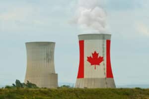 Two industrial cooling towers, one painted with a large Canadian flag and emitting steam, representing the Saskatchewan nuclear industry.