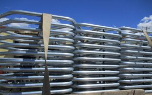 A stack of galvanised metal cattle panels, reflecting our tube and pipe bending capacity, secured with a tan nylon strap on a wooden pallet.